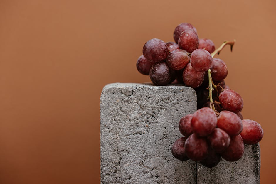 Juicy red grapes rest on a concrete block against a brown background.