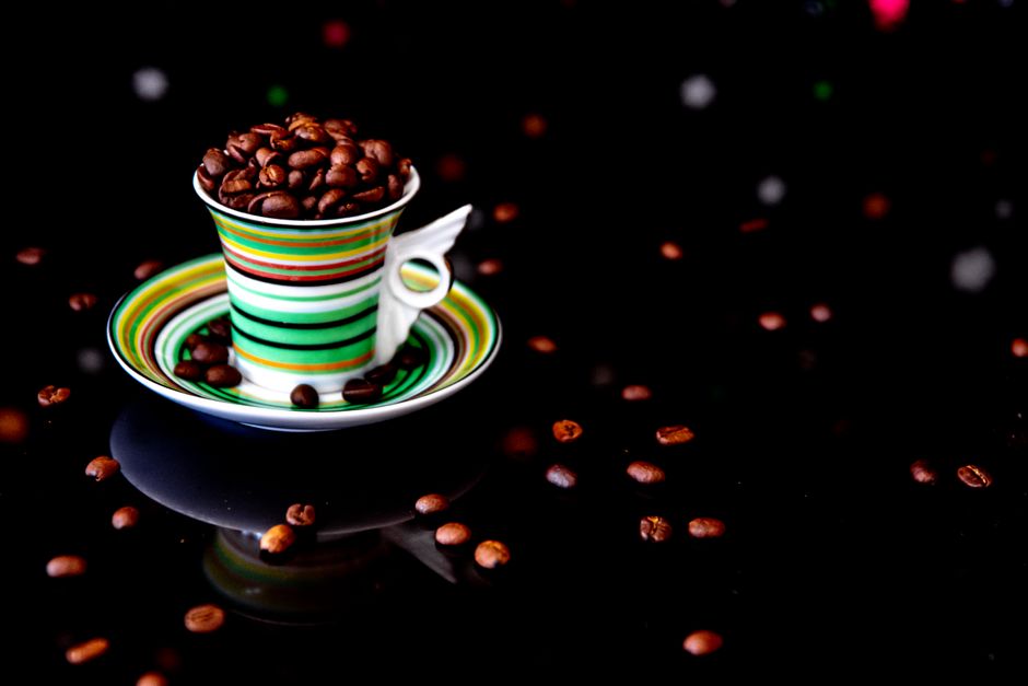 Vibrant striped cup overflowing with dark roasted coffee beans against a black background.