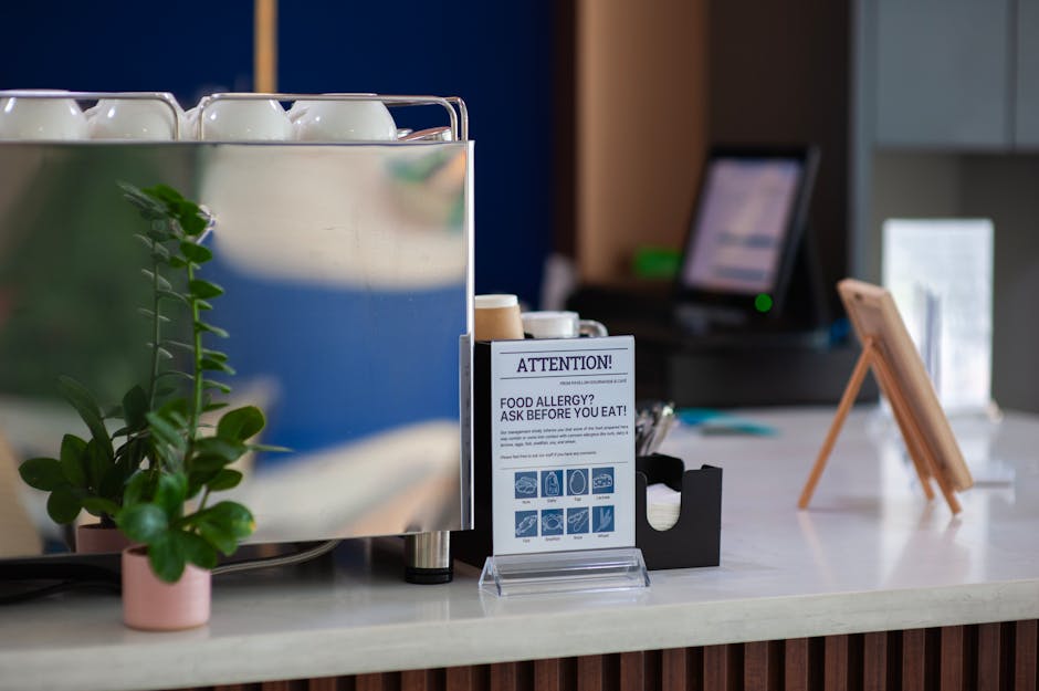 Coffee shop counter featuring an allergy warning sign and plant, highlighting food safety.
